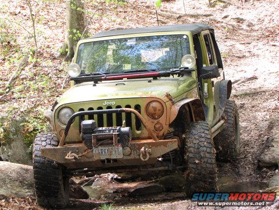 Green Jeep Wrangler with winch and off-road tires on a muddy trail. Virginia license plate RKGRVL