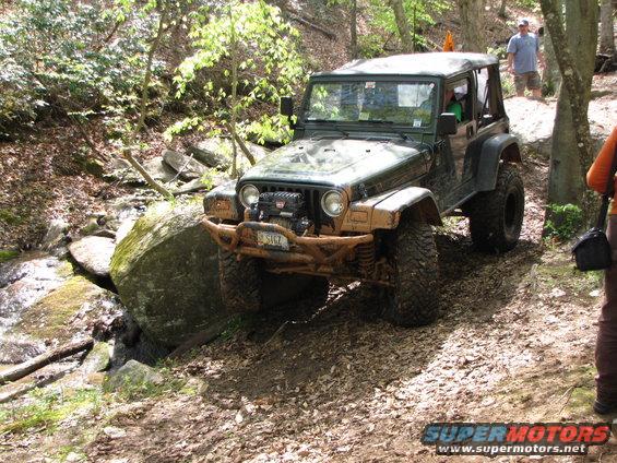 Green Jeep Wrangler off-roading over a large rock on a dirt path