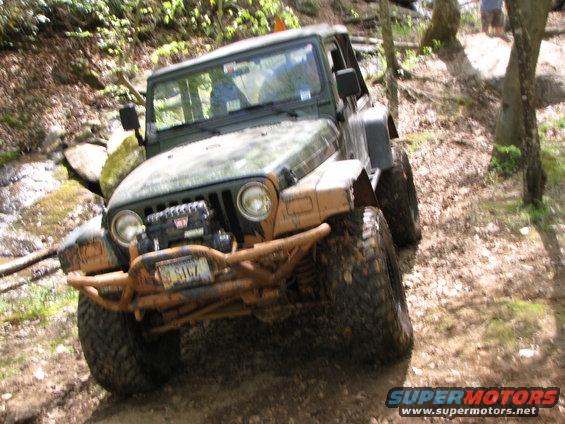 Green Jeep Wrangler with winch and off-road bumper navigating a muddy trail