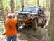 1979 Ford Bronco - Off-road Jeep Wrangler navigates a rocky obstacle on a wooded trail, with another vehicle in the background.