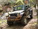 1979 Ford Bronco - A muddy Jeep Wrangler navigates a wooded trail with an orange flag visible on its antenna.