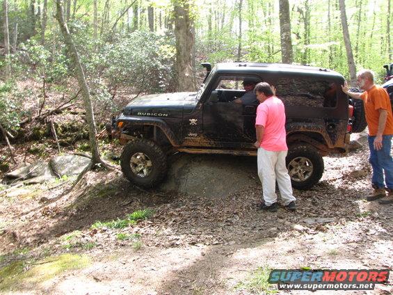 Black Jeep Wrangler Rubicon on rocky trail with people around. Another vehicle visible behind