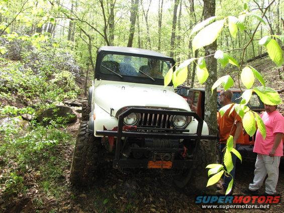 White Jeep CJ on a wooded trail with two people standing nearby