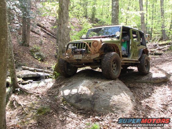 Green Jeep Wrangler driving over a large rock on a wooded trail