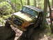 1979 Ford Bronco - A green Jeep Wrangler navigates a challenging off-road course, with one tire on a large rock and the vehicle angled against a tree.