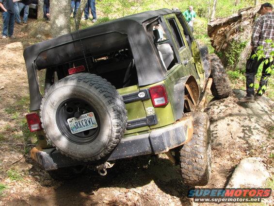 Green Jeep Wrangler with spare tire on rear, navigating rocky terrain