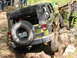 1979 Ford Bronco - A green Jeep Wrangler tackles a challenging off-road course, its spare tire prominently displayed on the rear.
