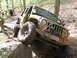1979 Ford Bronco - A Jeep navigates a rocky obstacle on a wooded trail, with another vehicle following behind.