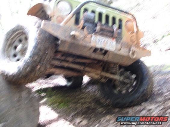 Mud-covered Jeep Wrangler with front tire on a rock, showing winch and grille