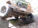 1979 Ford Bronco - A muddy Jeep Wrangler navigates an off-road obstacle, with its front tire climbing over a large rock.