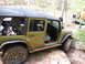 1979 Ford Bronco - A green Jeep Wrangler is shown off-roading with its doors removed, while other vehicles and people are visible in the background.
