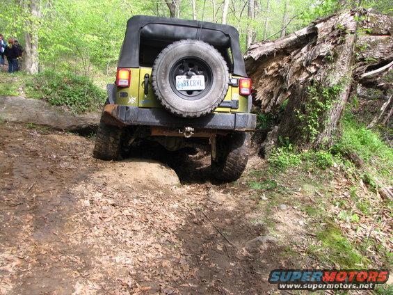 Yellow Jeep Wrangler driving on a dirt trail, going over a rock obstacle next to a fallen tree