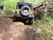 1979 Ford Bronco - A Jeep Wrangler navigates a challenging off-road trail with a fallen tree nearby.