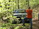 1979 Ford Bronco - A man in an orange shirt stands in front of a camouflaged Ford Bronco in a wooded area.