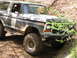 1979 Ford Bronco - This 1979 Ford Bronco is shown in a three-quarter front view, navigating an off-road trail with camouflage paint.