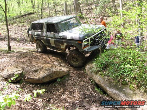 Camouflaged 1978 Ford Bronco navigating a rocky, wooded trail. FullsizeBronco.com sticker on windshield