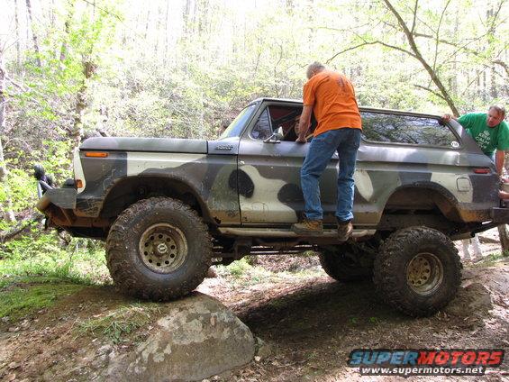 Camouflaged 1978 Ford Bronco off-roading with two men near the doors
