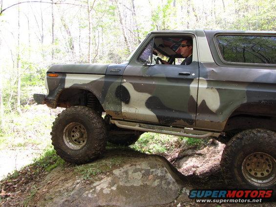 Camouflaged Ford Bronco with lifted suspension and large tires navigating rocky terrain