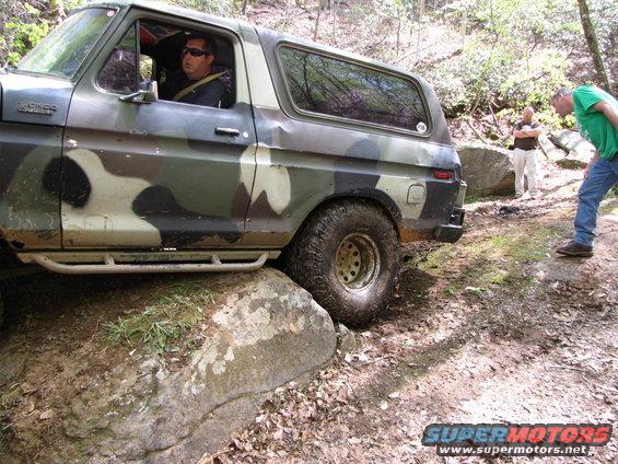 Man driving a camouflage 1979 Ford Bronco over rocks on a trail