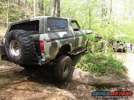 Camouflaged Ford Bronco with a spare tire on the back, driving off-road