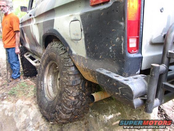 Man standing next to a camouflaged truck with large off-road tires and a custom bumper