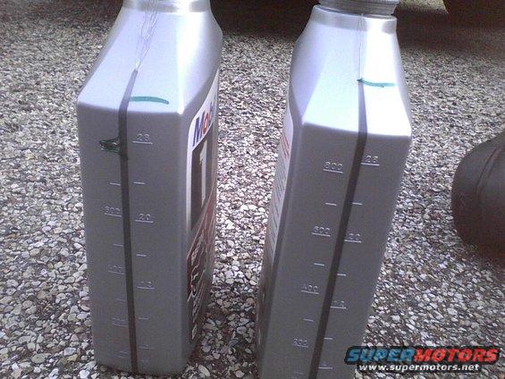 Two bottles of Mobil 1 oil sitting on gravel. One bottle has a green mark near the top