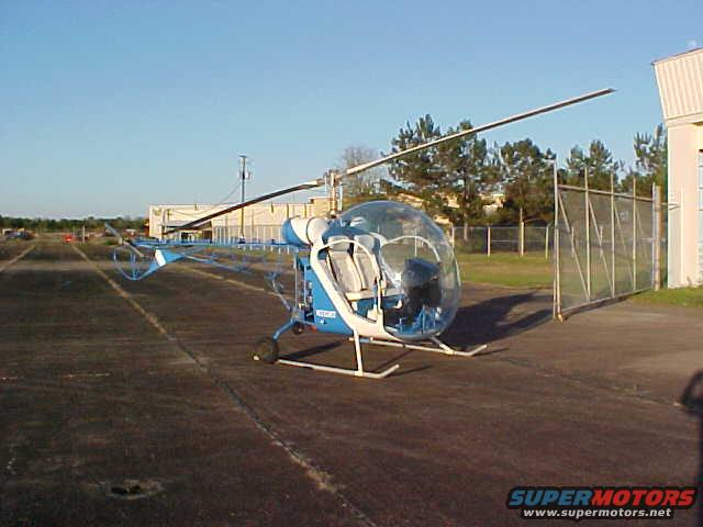 Blue and white helicopter with bubble canopy parked on asphalt