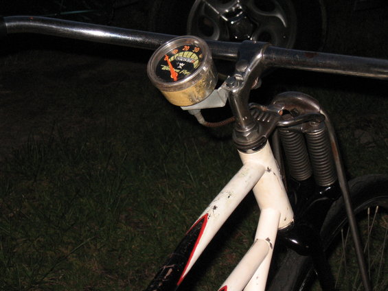 Bicycle handlebar with a speedometer gauge, chrome handlebars, and white frame with red and black accents