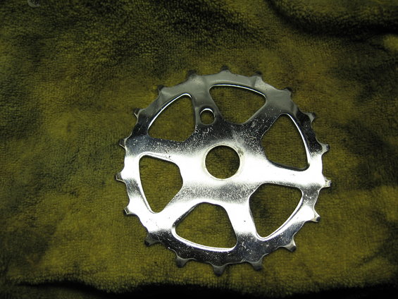 Chrome bicycle chainring with 5 large cutouts and 18 teeth, resting on a green cloth