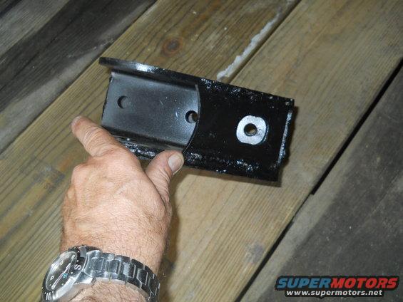 Hand holding a black metal bracket with two bolt holes and one washered bolt hole