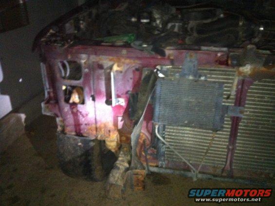 Damaged red vehicle front end with exposed radiator and engine components