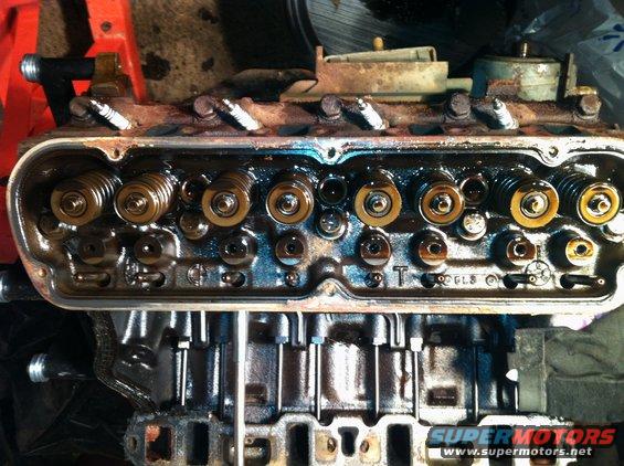 Engine cylinder head with visible valves and spark plug holes, showing oil residue
