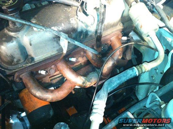 Close-up of an engine bay showing the exhaust manifold, spark plugs, and oil filter