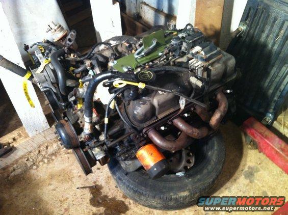Engine assembly resting on a tire, with various hoses and components attached
