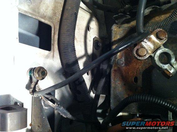 Close-up of engine bay wiring and a corroded battery terminal with black protective loom