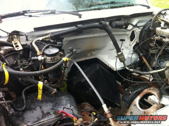 Engine bay with hoses, wires, and a black filter canister. Some yellow tags are visible on hoses
