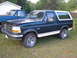 1993 Ford Bronco - A dark green and white Ford Bronco is parked on a grassy area next to a blue pickup truck.