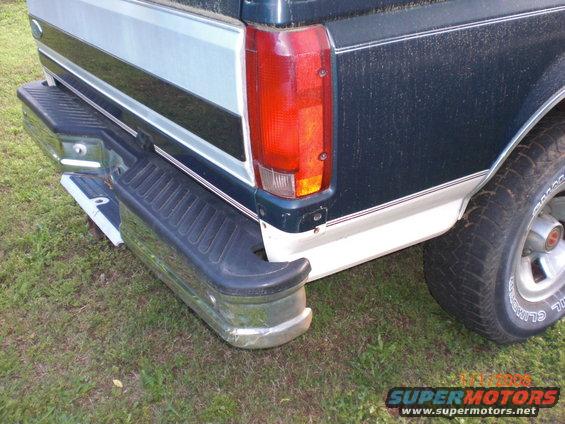 Dark green and white pickup truck rear bumper and taillight, chrome step bumper, grass background