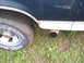 1993 Ford Bronco - Detail shot of a vehicle's rear wheel and exhaust pipe, with a white stripe along the lower body.