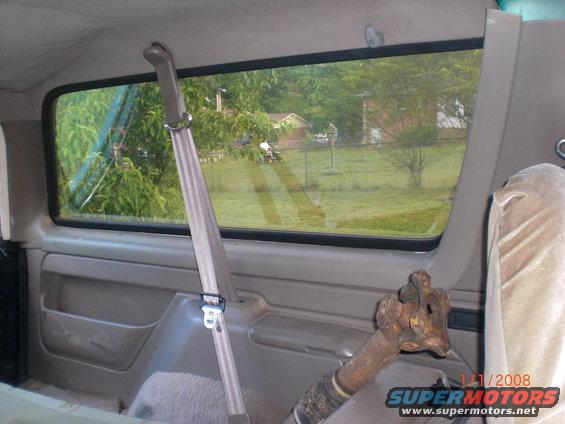 Interior view of a vehicle showing a seatbelt and a rusty pipe, with a rural scene outside