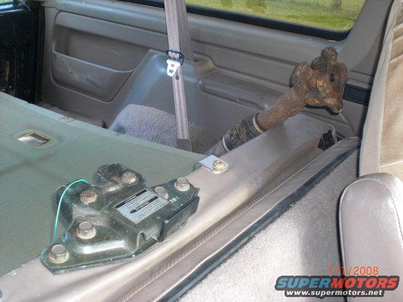 Interior view of a vehicle showing a rusty driveshaft and a black mounting bracket with a green wire
