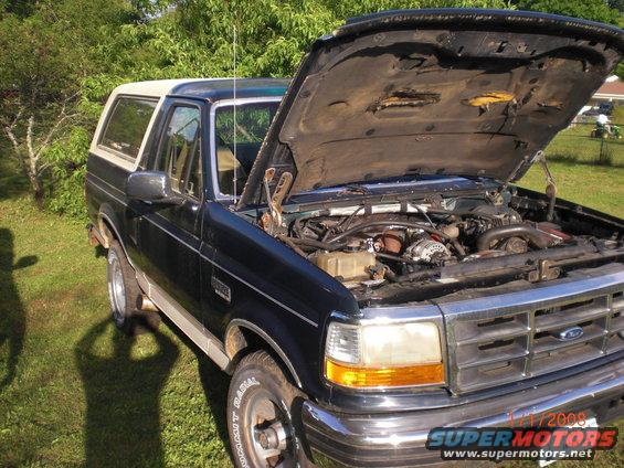 1993 Ford Bronco, dark blue with tan top, hood open showing engine. Parked on grass