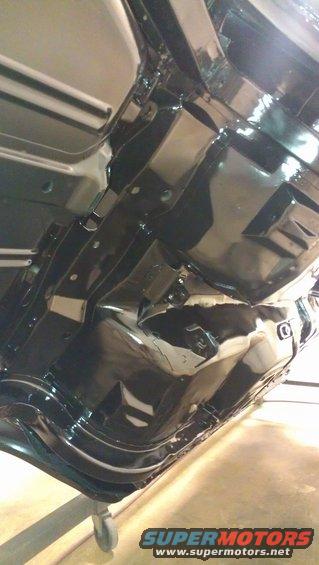 Undercarriage of a black vehicle, viewed from below and to the side, showing frame rails and suspension components
