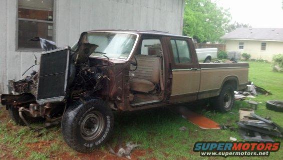 Damaged pickup truck with front end missing, doors open, parked in a yard