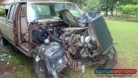 pickup truck with front end damage, engine exposed, sitting in a grassy area