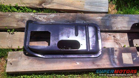 Dark blue car door panel with square and oval cutouts, resting on wooden planks