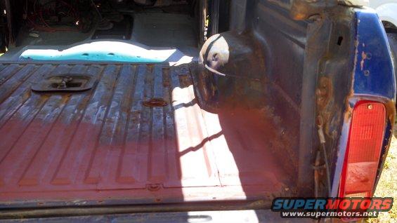 1979 Ford Bronco truck bed with red primer and rust, showing a tie-down anchor and a taillight