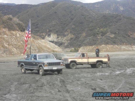 blue and brown pickup trucks in mud, American flag on blue truck