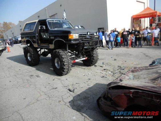 Lifted black Ford Bronco with a tan top, custom bumper, and large tires parked next to a crushed car