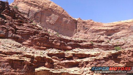 Layered red rock cliffs under a clear blue sky. A watermark reads 'SUPER MOTORS www.supermotors.net'